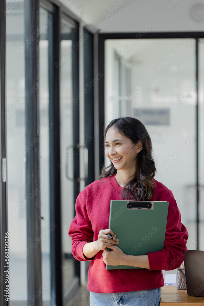 Happy smiling young asian business woman holding digital tablet standing in the office,