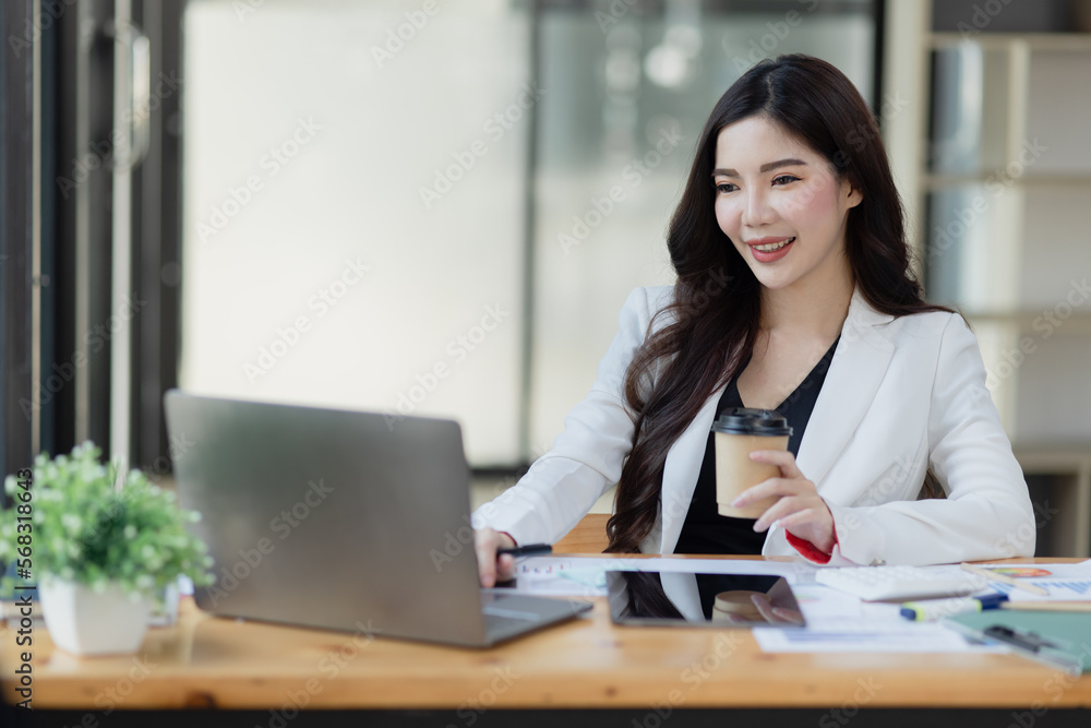 Joyful Asian businesswoman freelancer entrepreneur smiling and rejoices in victory while sitting at desk in office.