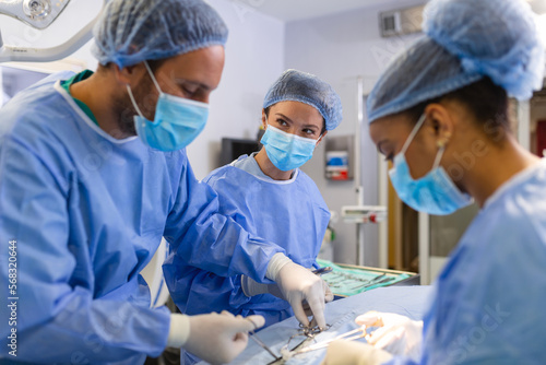 Multi-ethnic healthcare workers performing surgery on patient at operation theater. Medical colleagues operating in emergency room at hospital. They are in scrubs