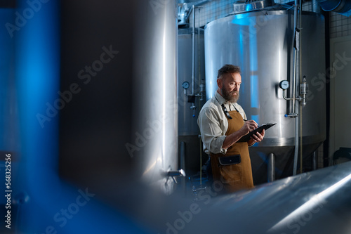 Картината върху платно Handsome bearded man brewer inside modern beer factory around steel tanks