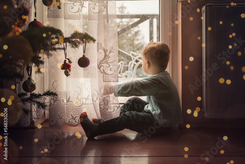 Toddler boy sitting on the floor by the window next to a christm photo