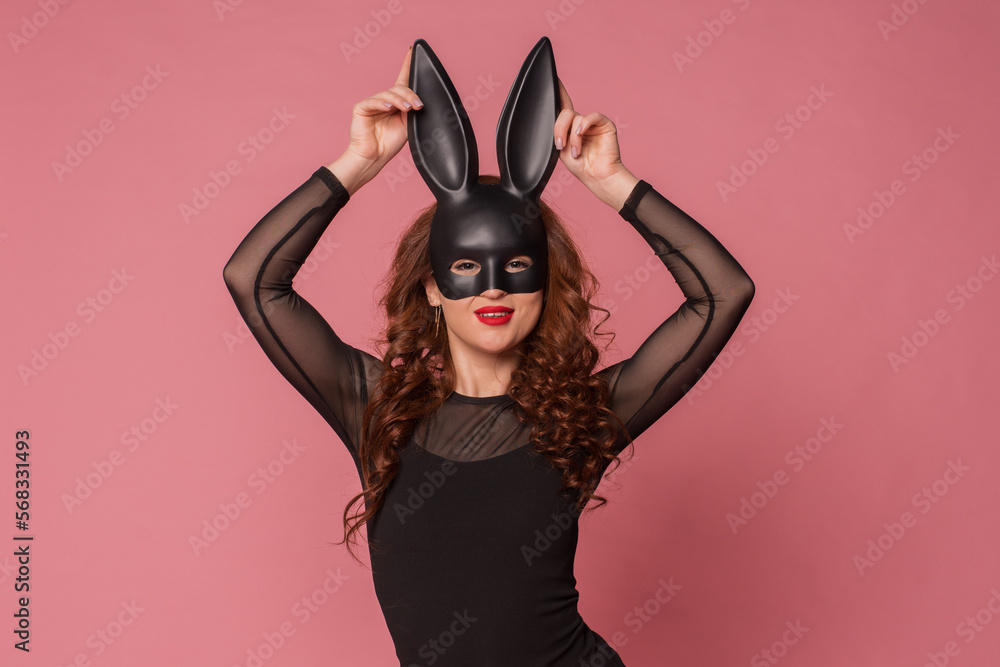 a girl with red hair posing in a black dress and black bunny ears on a pink background.Easter bunny concept. Naughty girl. Halloween costume. a girl with red hair posing in a black dress and black bunny ears on a pink background.Easter bunny concept. Naughty girl. Halloween costume.