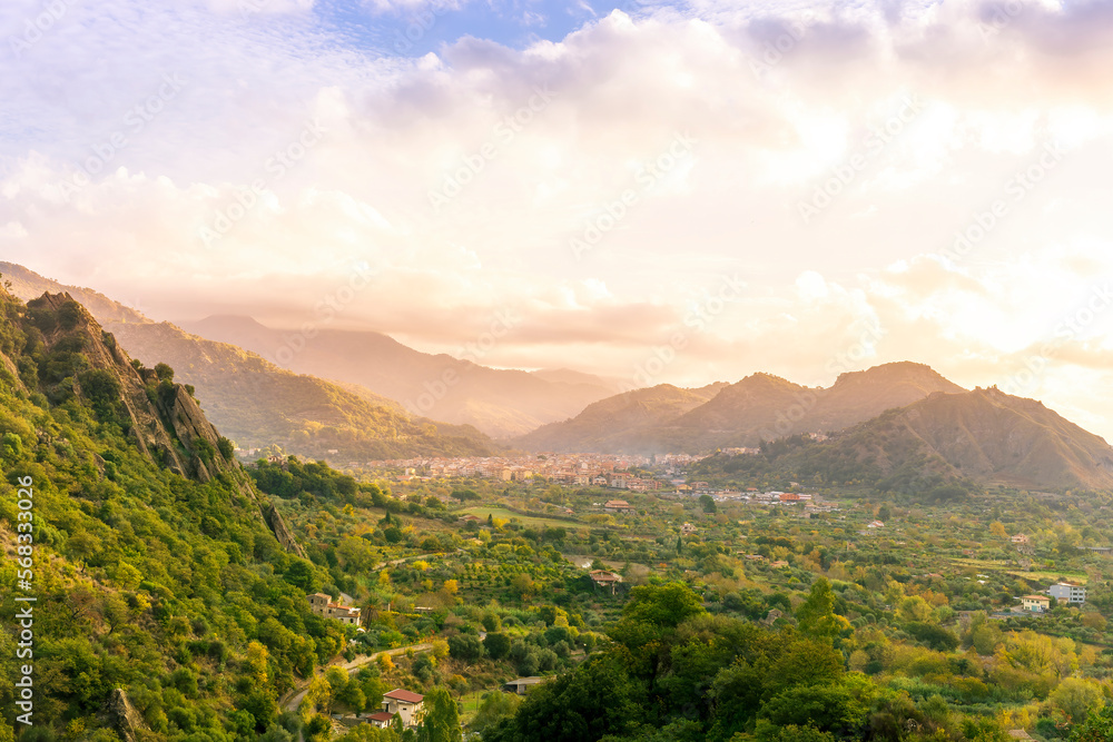 Naklejka premium amazing sunset or sunrise in a mountain valley among slopes and hills with picturesque town on a rocky plato and nice cloudy sunset on background