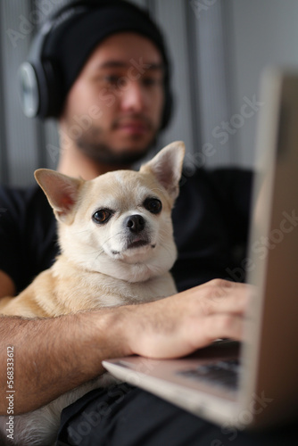 A stylish guy dressed in black clothes, with headphones, at home with his dog, work on a laptop, play board games, spend time together. The guy works on-line, makes purchases on a laptop, IT