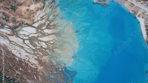 Top view of the turquoise water of a mountain lake. Clean clear water with streaks on the bottom. Patterns from a mountain river. The color shimmers from blue-green to blue. Trees in the water. Issyk