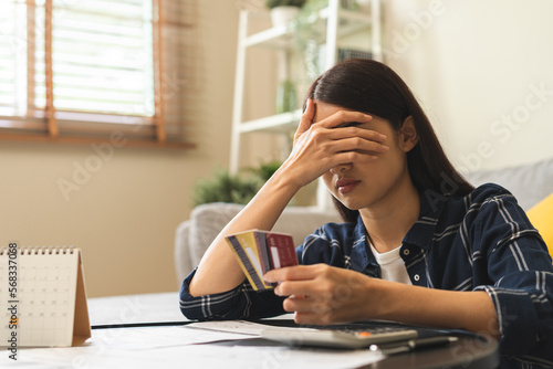 Business financial concept, owe asian young woman, female sitting cover face with hands, stressed by calculate expense from invoice or bill, have no money to pay mortgage or loan. Debt, bankruptcy. photo