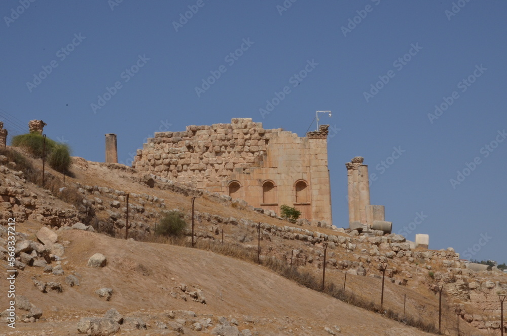 Fototapeta premium Sunny temples, arches, the Nymphaeum, stone ornaments, columns and column bases on the ruins of the city of Jerash in Jordan.