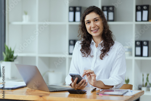 Businesswoman using smartphone and laptop computer working at desk in office.