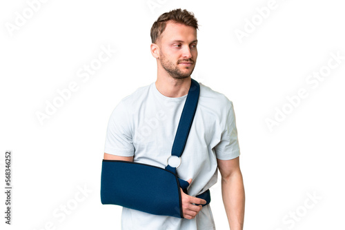 Young caucasian man with broken arm and wearing a sling over isolated chroma key background looking to the side photo