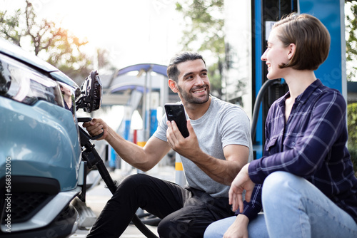 Couple travel lover, Man holding a DC - CCS type 2 EV charging connector at EV charging station with his car, man preparing an EV - electric vehicle charging connector for recharge a vehicle by smartp