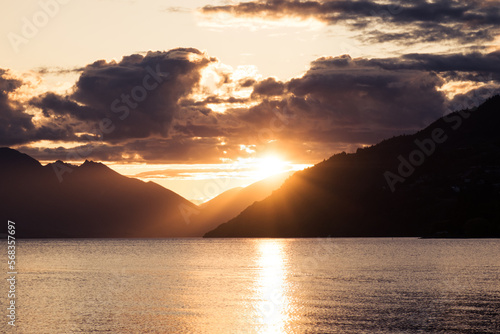 Sun breaking through the clouds over the distant mountains and reflecting on Lake Wakatipu on the South Island of new Zealand