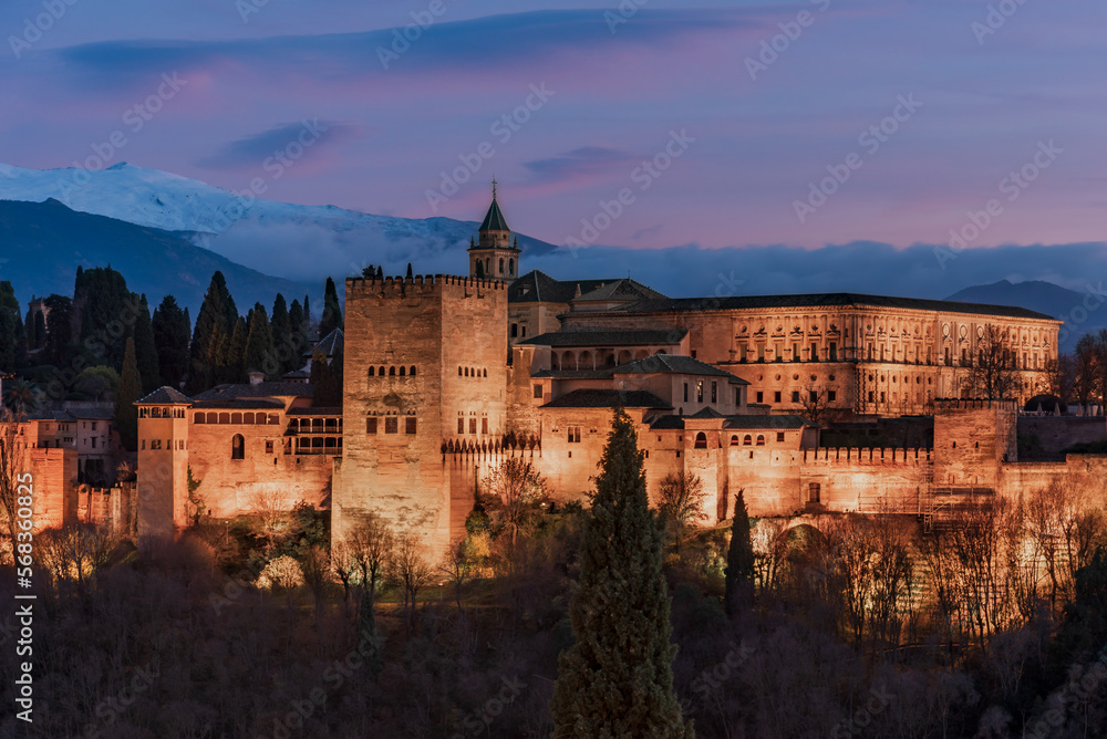 Palace of Carlos V in the Arab complex of the Alhambra in Granada with its illumination at blue hour, with Sierra Nevada in the background.
