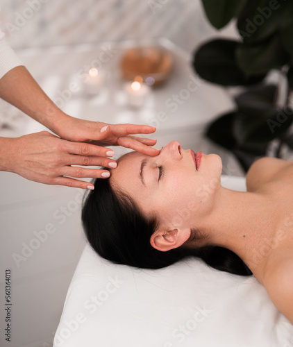 Crop therapist massaging forehead of relaxed female client in salon