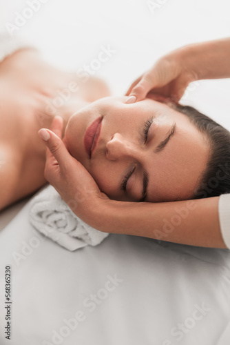 Young woman lying with closed eyes during face massage in beauty salon