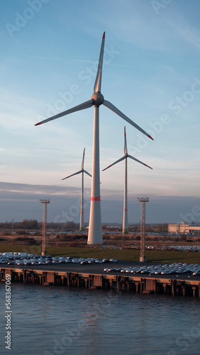 Emden, Germany - 02 04 2023: Parking place with the brand new vehicles in the area of the biggest german car manufacturer with huge wind generators in the background © Andriy Sharpilo