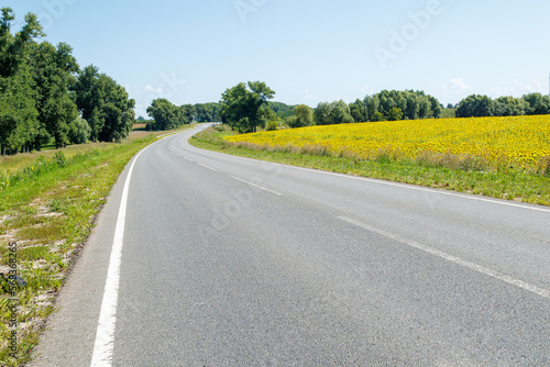 Asphalt road in the countryside on a sunny summer day. A highway and a field of blooming sunflowers on a sunny spring day.