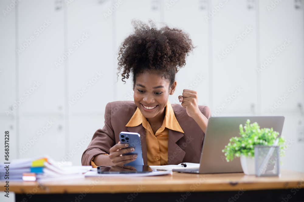Young African American woman very happy and excited doing winner gesture with arms raised at table office, Business success and celebration concept. Young African American woman very happy and excited doing winner gesture with arms raised at table office, Business success and celebration concept.
