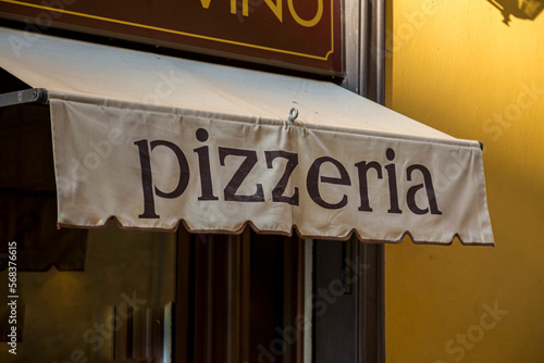 A Pizzeria Awning with the word pizzeria on a facade of a restaurantin Italy.