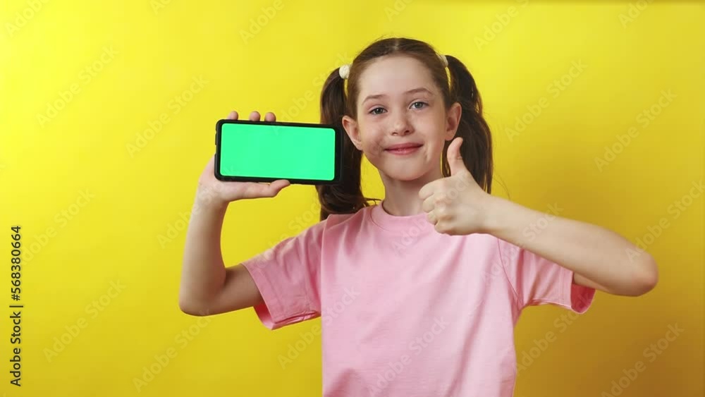Happy smiling little girl showing smartphone with blank green screen, display mockup for advertising text, 4K Happy smiling little girl showing smartphone with blank green screen, display mockup for advertising text, 4K