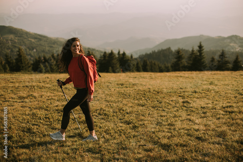 Young woman is taking a scenic hike on a hill, carrying all her necessary gear in a backpack
