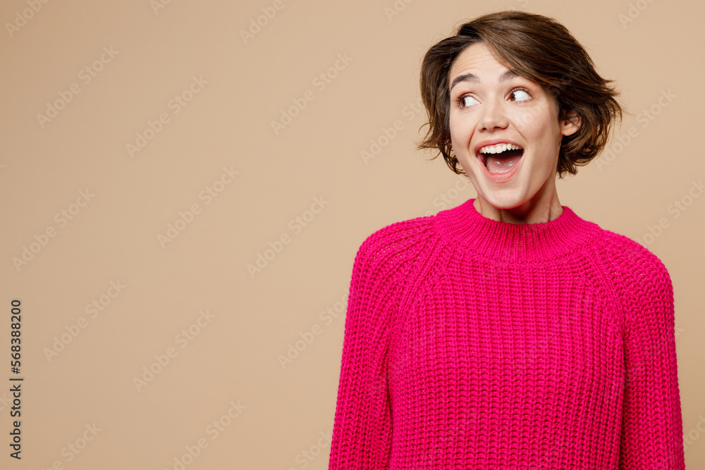 Young surprised shocked excited happy caucasian woman wear pink sweater look aside on workspace area mock up isolated on plain pastel light beige background studio portrait. People lifestyle concept. Young surprised shocked excited happy caucasian woman wear pink sweater look aside on workspace area mock up isolated on plain pastel light beige background studio portrait. People lifestyle concept.