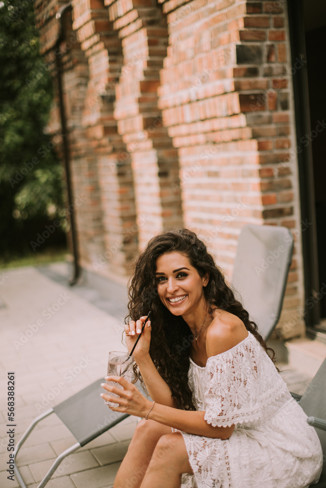 A young woman with curly hair relaxes on a deck chair and enjoys a glass of fresh lemonade A young woman with curly hair relaxes on a deck chair and enjoys a glass of fresh lemonade