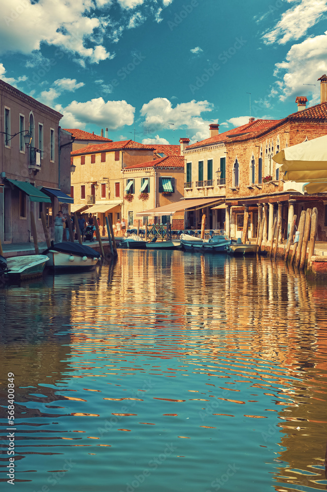 Island Murano in Venice, Italy. Scenic view of canal with boats at the docks on water. Picturesque landscape traditional mediterranian architecture houses. Cosy street motley buildings