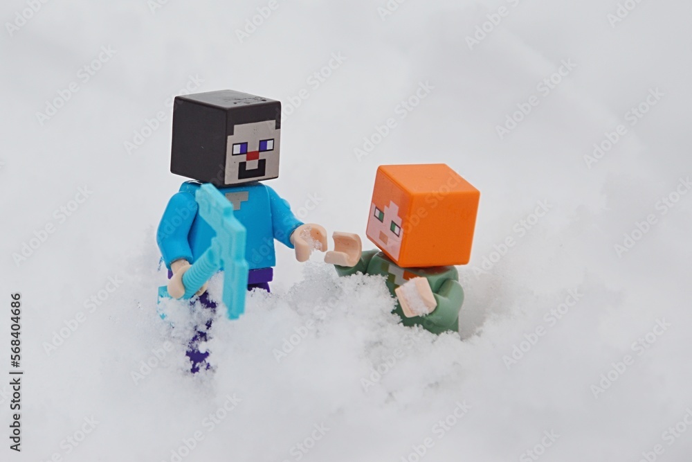 Naklejka premium LEGO Minecraft figure of Steve with diamond pickaxe helping Alex out of deep snow after avalanche.