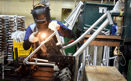 Industrial worker doing welding of a bicycle manufacturing industry. Workers wear work safety uniforms and wear anti-radiation helmets