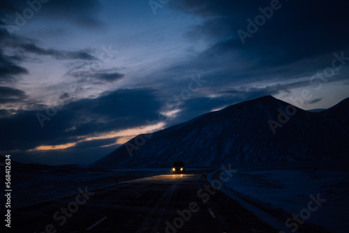 Fototapeta Naklejka Na Ścianę i Meble -  Highway in iceland with car coming from the front with headlights on and with snowy mountain in the background at dusk