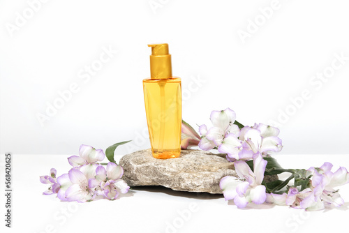 A transparent bottle of oil for sun protection  tanning or hair care  on a podium pedestal. White gray background with hard shadows  flowers and plants. Cosmetics for summer care.
