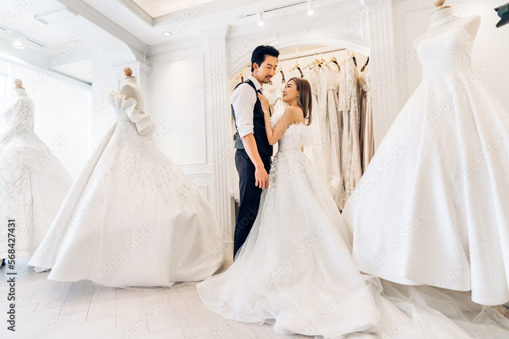Naklejka premium Portrait of smiling cheerful happy love asian couple fashion bride man and woman posing in white wedding dress for pre wedding hug together at wedding interior fashion studio