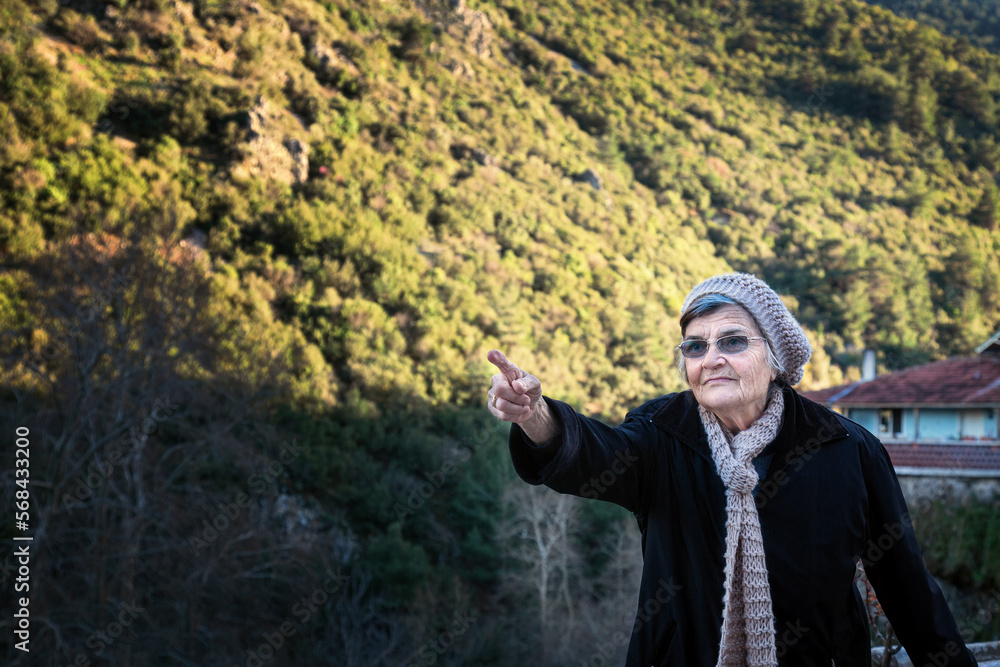 Elderly woman in black jacket and hat pointing at the mountains Elderly woman in black jacket and hat pointing at the mountains