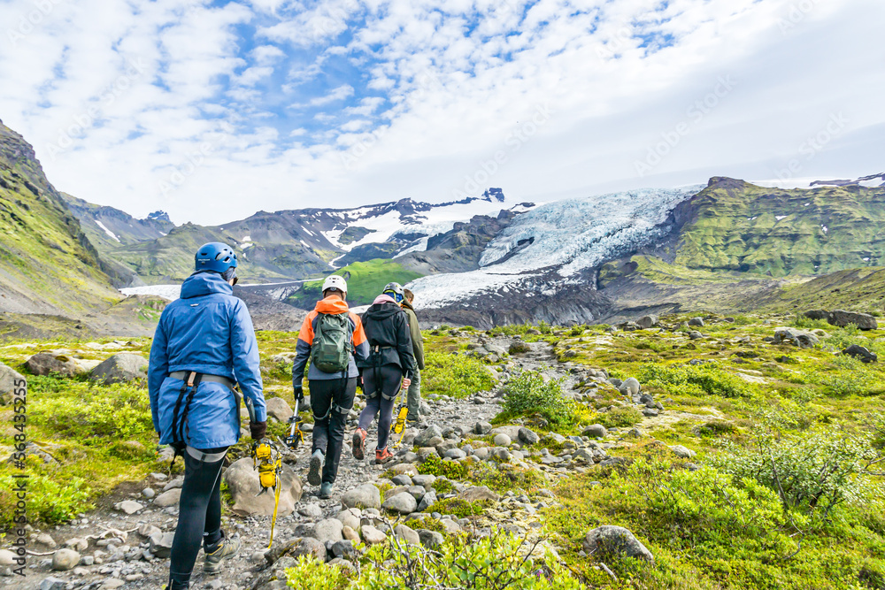 Group of tourists walking on narrow path to glacier for glacier tour and expedition. Tour members wearing helmet and full gear to climb glacier. Glacier, ice and mounts ins in background.