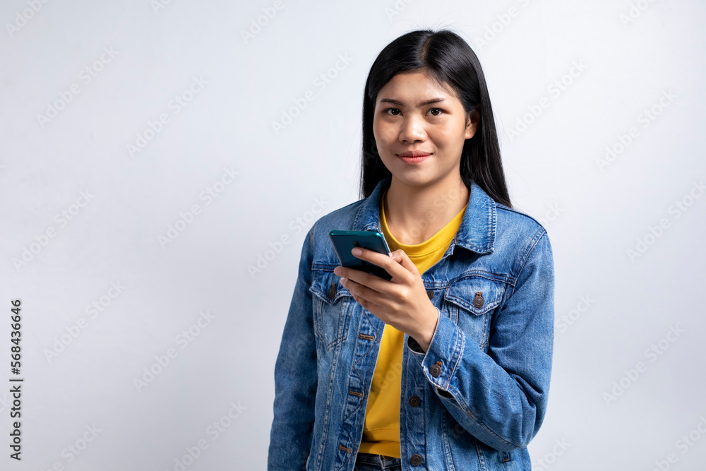 Asian teenage girl wearing jeans talking and texting on the smartphone isolated in white background and looking at camera Asian teenage girl wearing jeans talking and texting on the smartphone isolated in white background and looking at camera