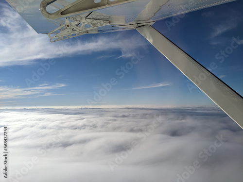 Window view from light general aviation aircraft. Strut and wing of semi-cantilever high-wing airplane flying over the clouds on a sunny day. photo