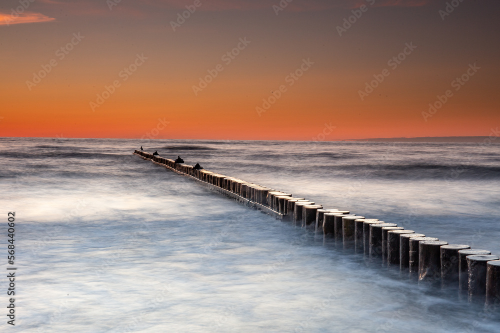 Sunset on the Baltic Sea in Rowy, Poland. Landscape with waterbreak in the sea under the sky at sunset.