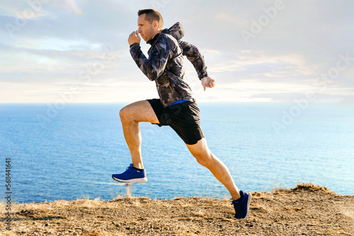 male runner in windbreaker running in background sky and sea
