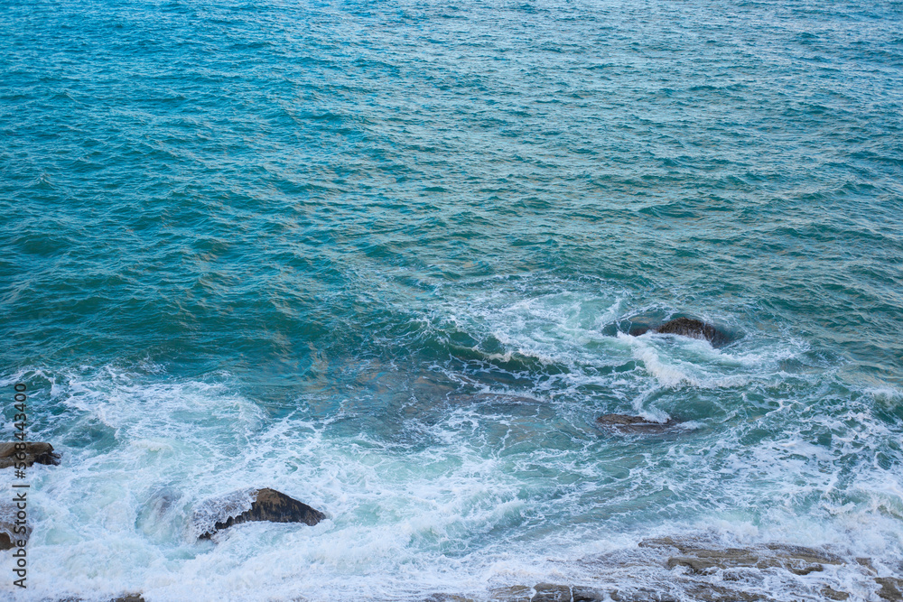 Obraz premium The surface of the sea with the wave and the stones on the shore, top view. Sea blue background