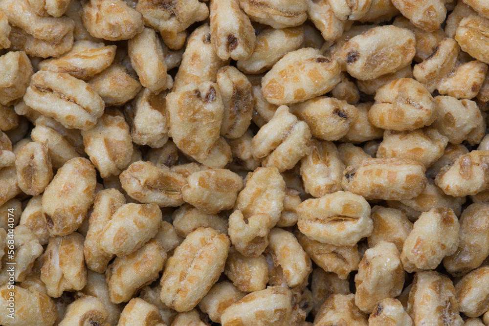 Dry honey puffed wheat cereal pieces scattered loosely directly above. Breakfast foods textured background, full frame image. Dry honey puffed wheat cereal pieces scattered loosely directly above. Breakfast foods textured background, full frame image.