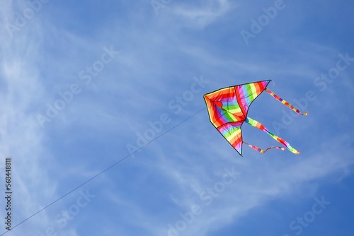 rainbow colored kite flying high in the blue sky with some white clouds
