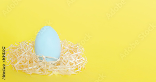 Banner. Easter egg, feathers in a nest on yellow background. The minimal concept. Top view. Card with a copy of the place for the text.