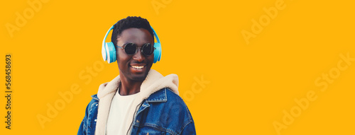 Portrait close up of happy smiling young african man in wireless headphones listening to music looking away isolated on yellow background