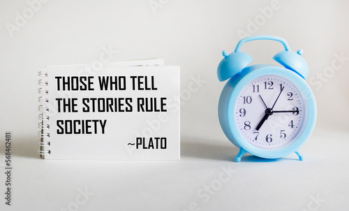 Those who tell stories rule society, Plato quotes the ancient Greek philosopher. Inspirational handwriting on notepad on white background with clock, storytelling concept photo