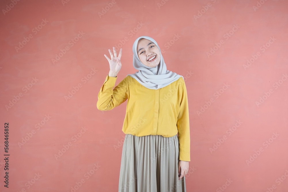 Fototapeta premium Beautiful Asian woman in yellow shirt and hijab showing and pointing up with finger number four while smiling confident and happy on brown background