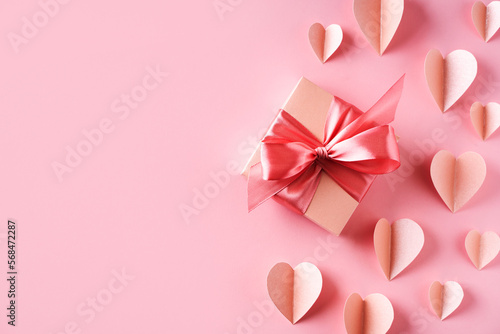 Pink gift box with bow and paper hearts on pink background