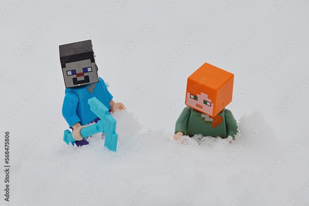 Naklejka premium LEGO Minecraft figures of Steve and Alex climbing on snowy hill, winter cloudy sunshine.