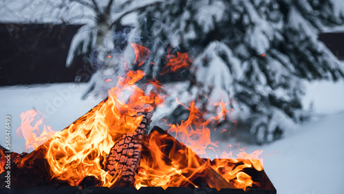 Firewood is burning in the grill. Fire on the background of snow. Heat and cold. Flames.
