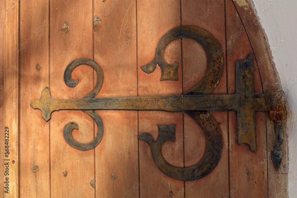 Decorative rustic metal hinge on old wooden door on a stone building. Decorative rustic metal hinge on old wooden door on a stone building.