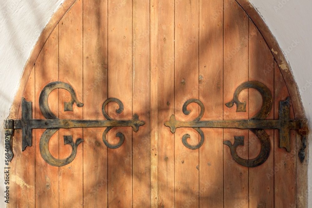 Decorative rustic metal hinges on old wooden doors on a stone building. Decorative rustic metal hinges on old wooden doors on a stone building.